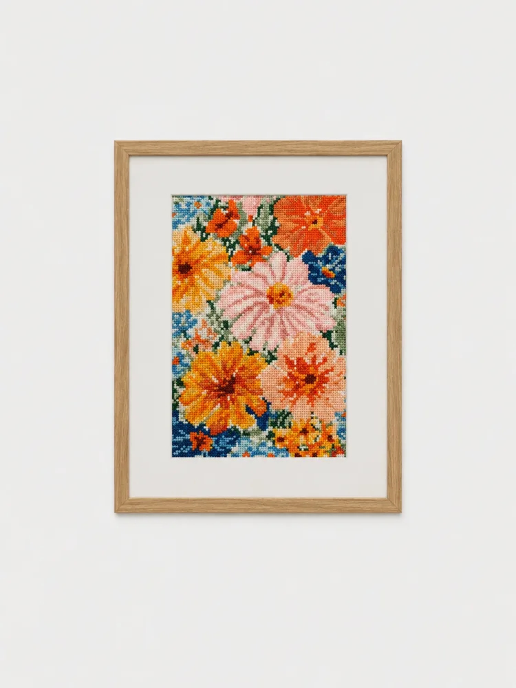 Quadro bordado em ponto cruz com margaridas rosa, flores laranja e amarelas sobre fundo azul
